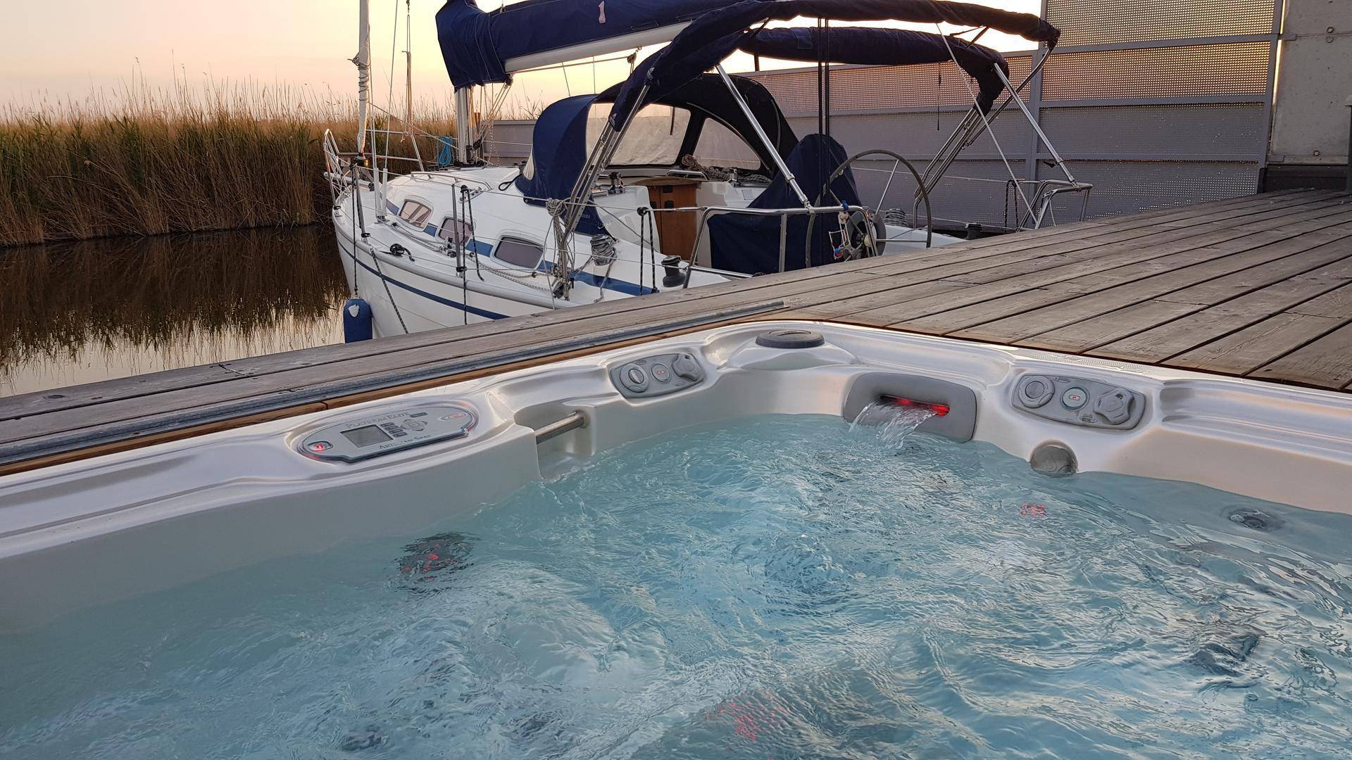 Whirlpool auf einer Holzterrasse neben einem Segelboot bei Sonnenuntergang.