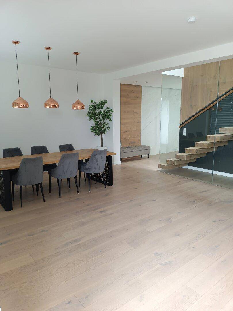 Heller Essbereich mit Holztisch, modernen Pendelleuchten und offener Treppe.