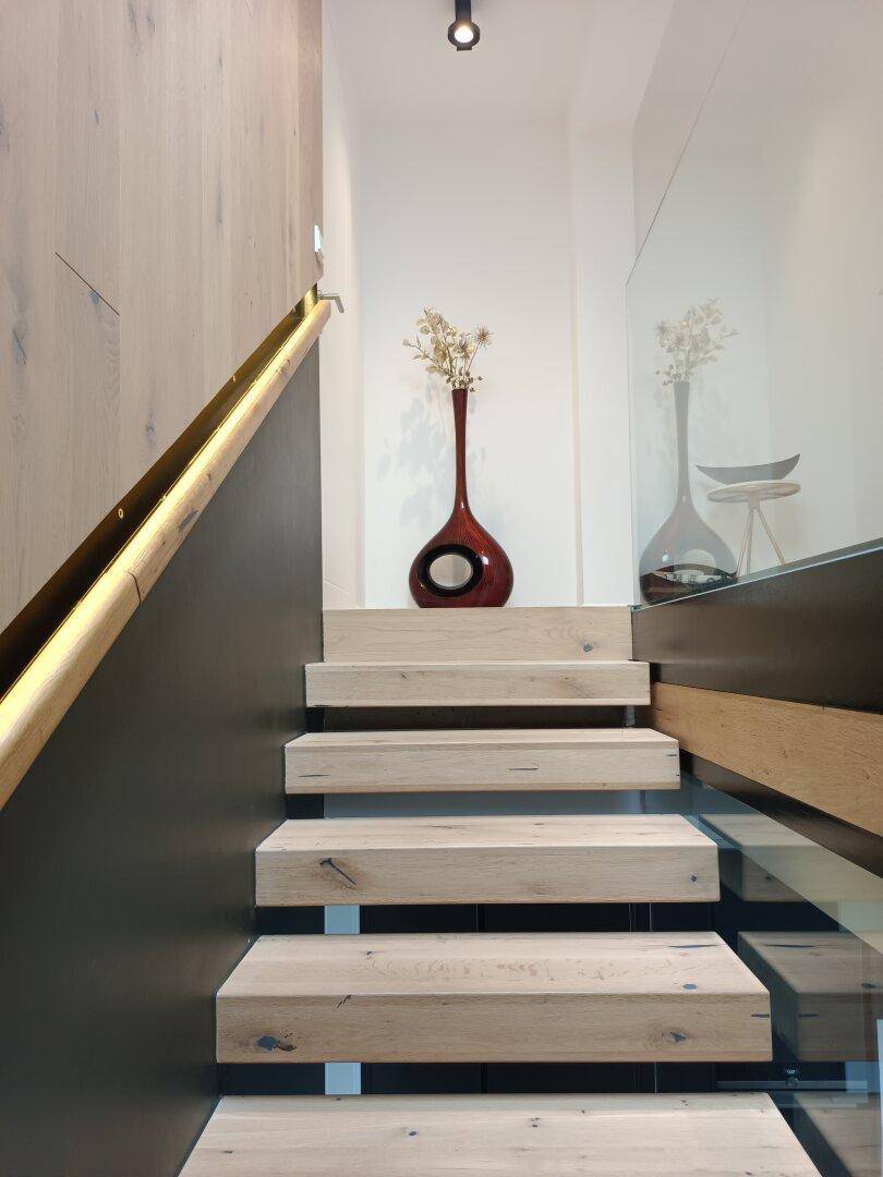 Moderne Holztreppe mit Glasgeländer und indirekter Beleuchtung, verziert mit einer Vase.
