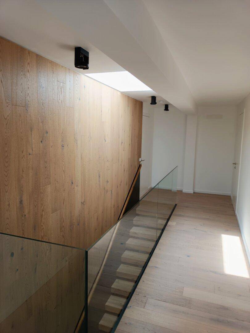 Heller Flur im Obergeschoss mit Holzwand, Glasgeländer und natürlichem Lichteinfall.