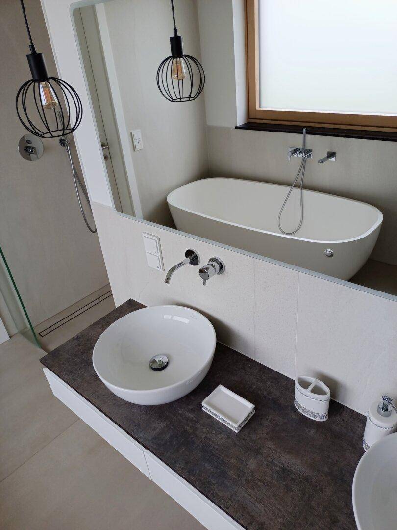 Modernes Badezimmer mit freistehender Badewanne, Aufsatzwaschbecken und Fenster.