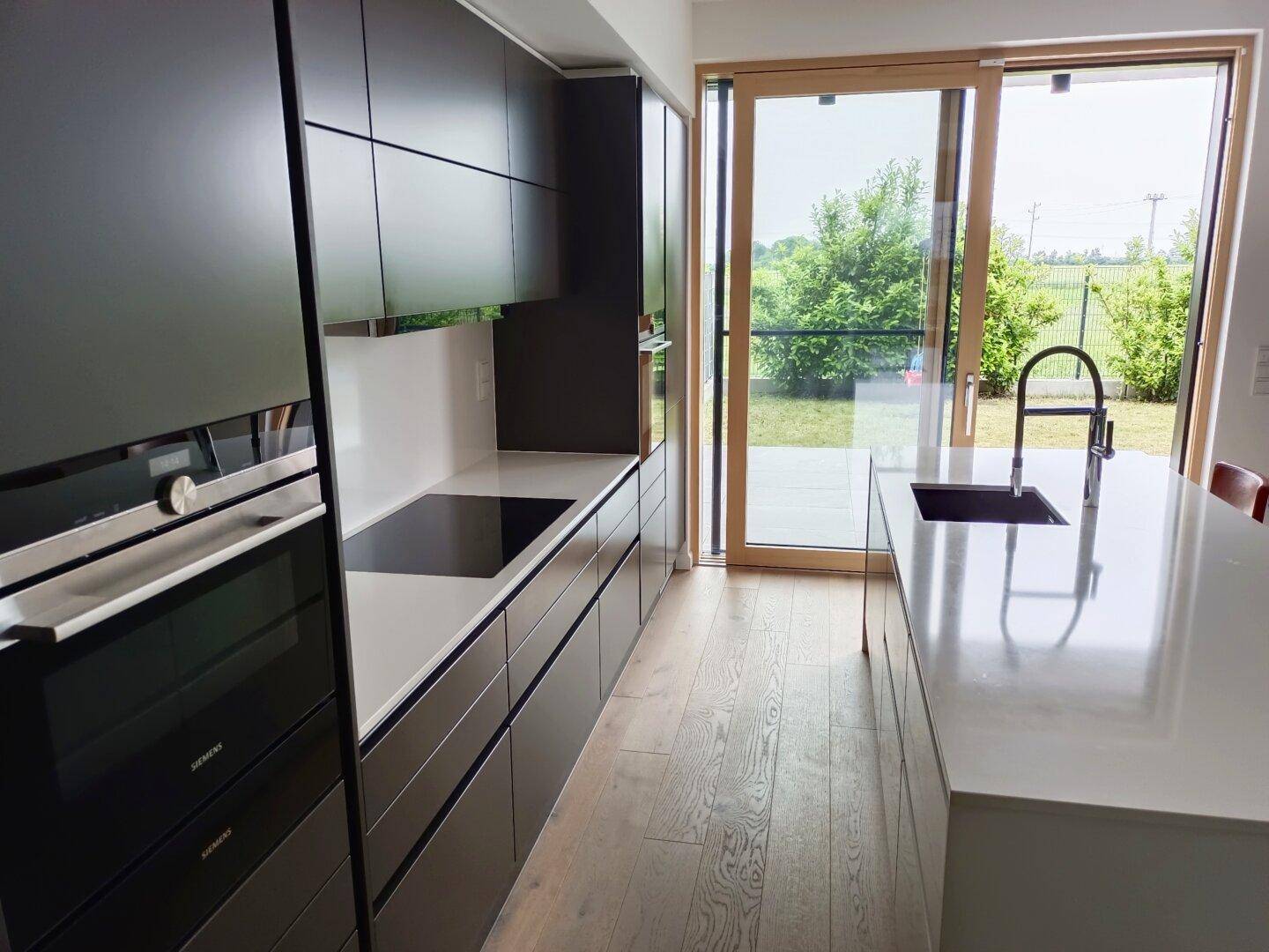 Moderne Küche mit dunklen Schränken, heller Arbeitsplatte und Blick in den Garten.