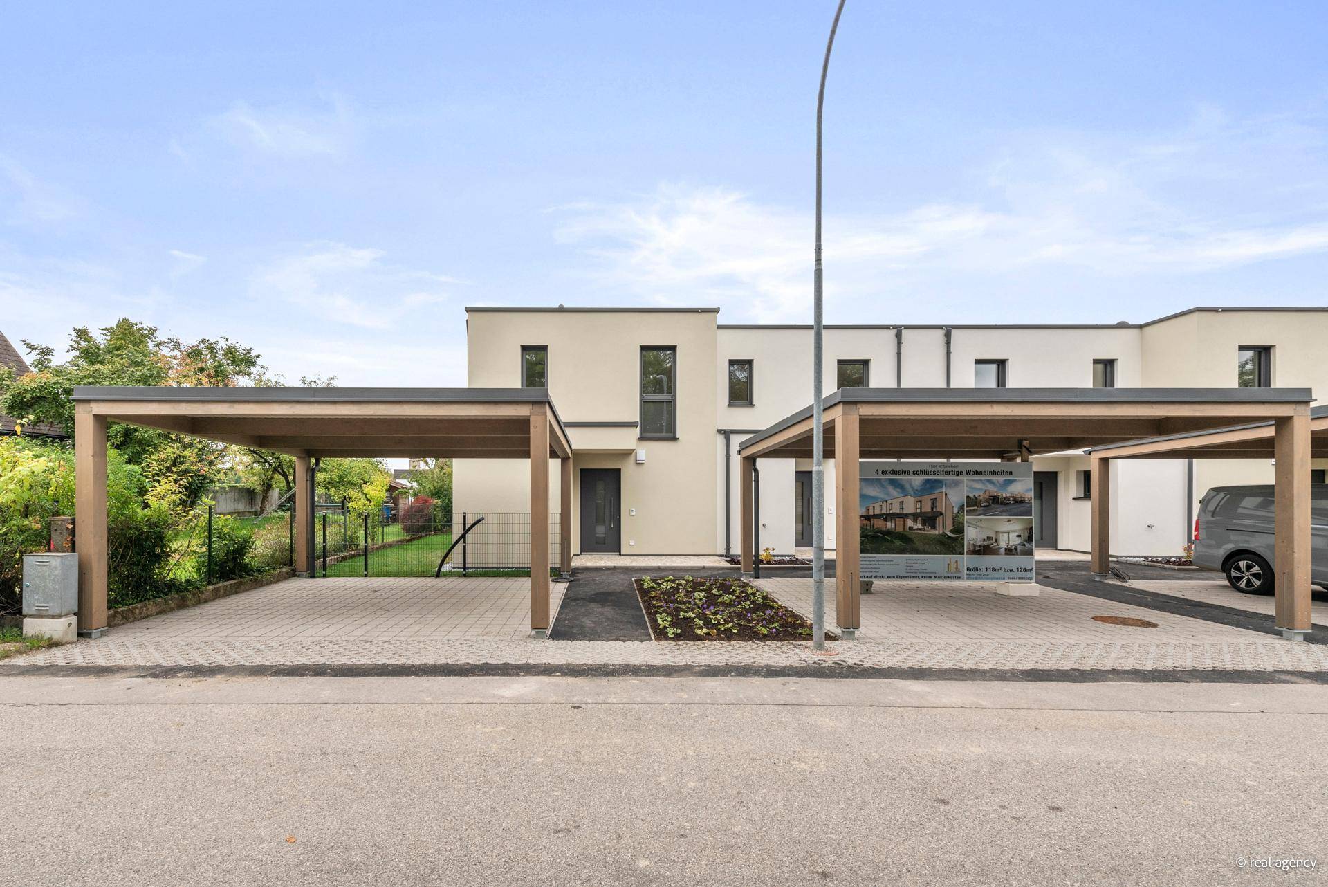 Ansicht der modernen Reihenhäuser mit Carports und gepflegter Außenanlage an einem sonnigen Tag.