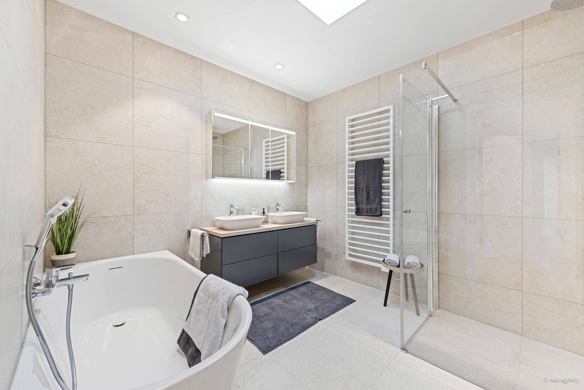 Luxuriöses Badezimmer mit Badewanne, Doppelwaschbecken, großer Dusche und viel Tageslicht.