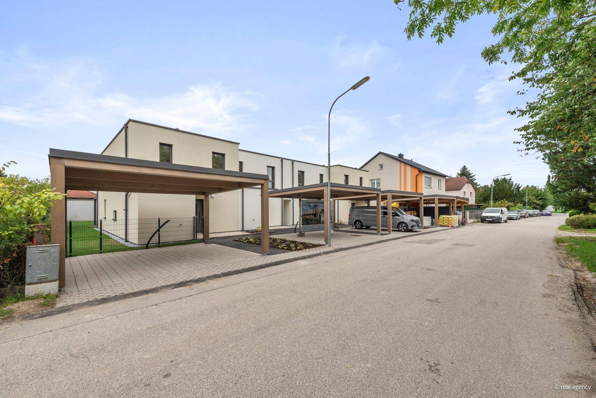 Reihenhäuser mit Carports in einer ruhigen Wohnsiedlung, umgeben von Grünflächen und weiteren Häusern.