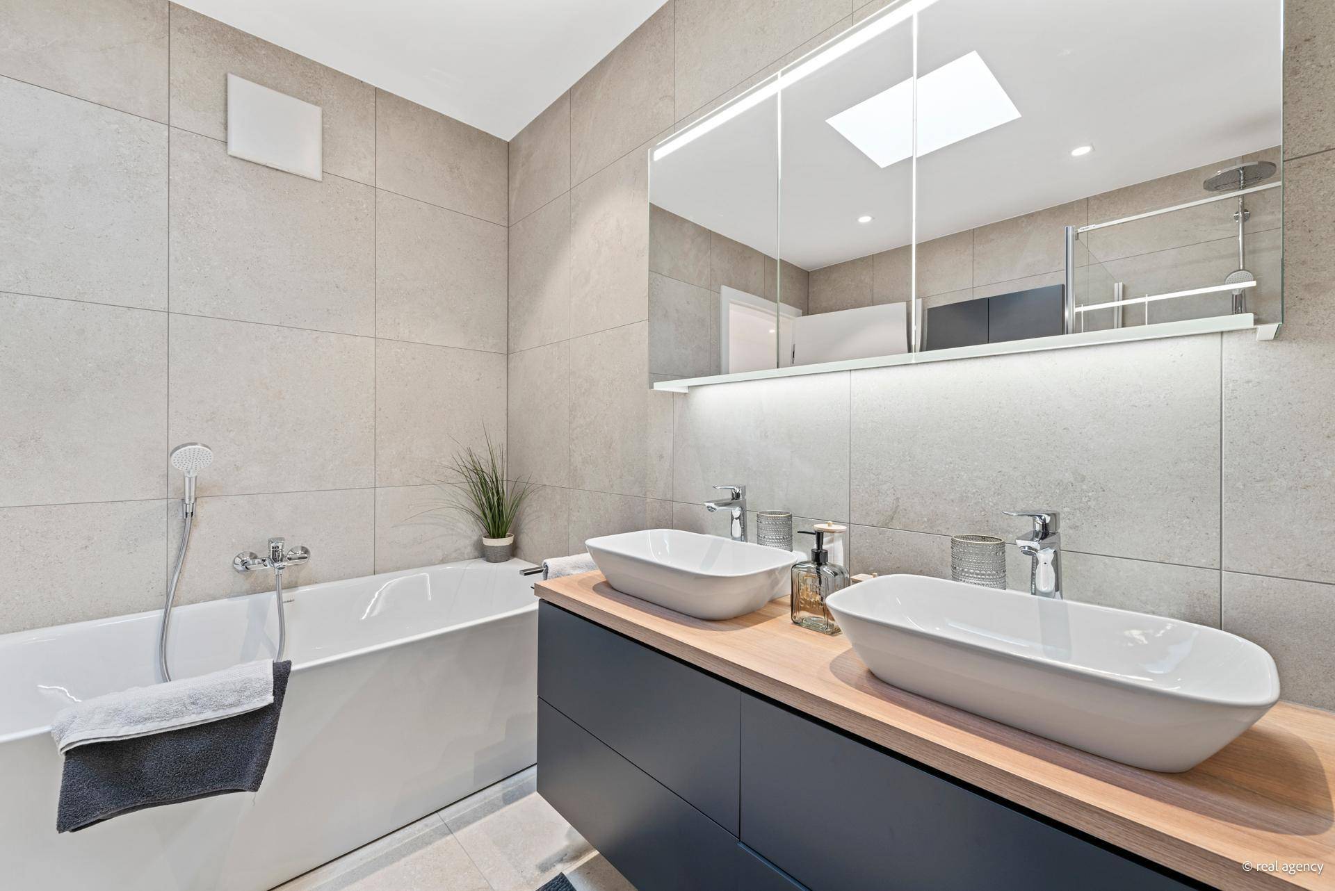 Geräumiges Badezimmer mit Badewanne, Doppelwaschbecken und viel Tageslicht durch ein Dachfenster.