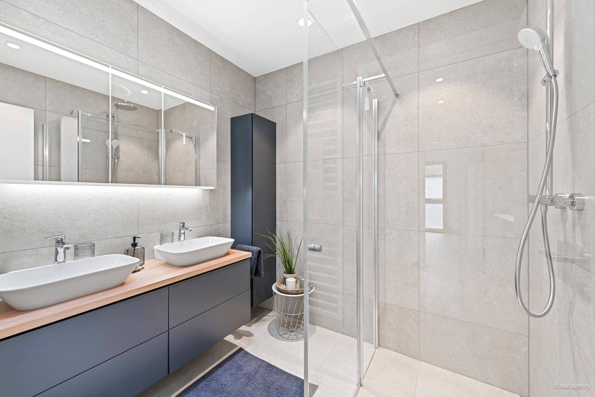 Geräumiges Badezimmer mit Doppelwaschbecken, begehbarer Dusche und stilvollen grauen Fliesen.