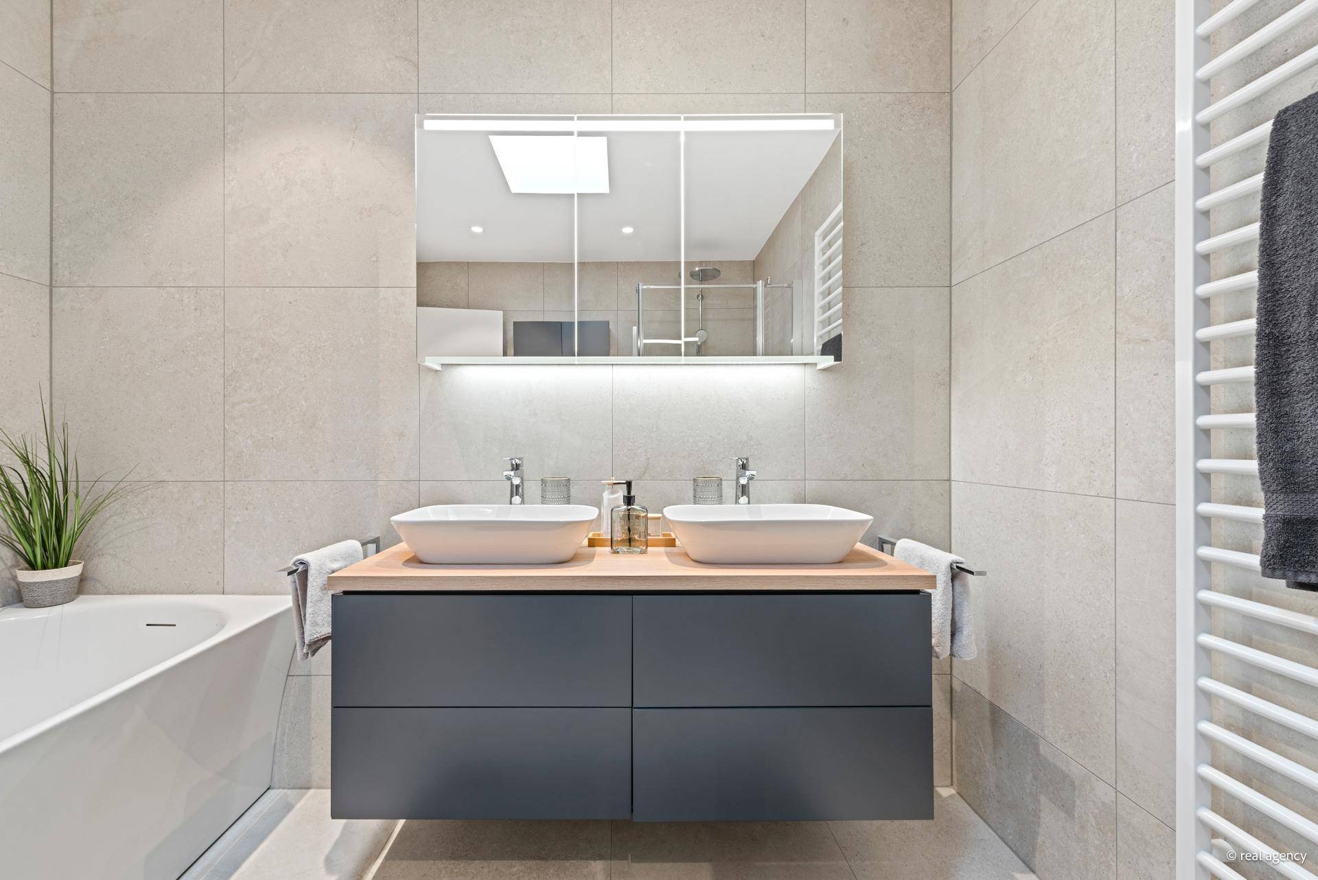 Helles Badezimmer mit Badewanne, Doppelwaschbecken und natürlichem Licht von oben durch ein Dachfenster.