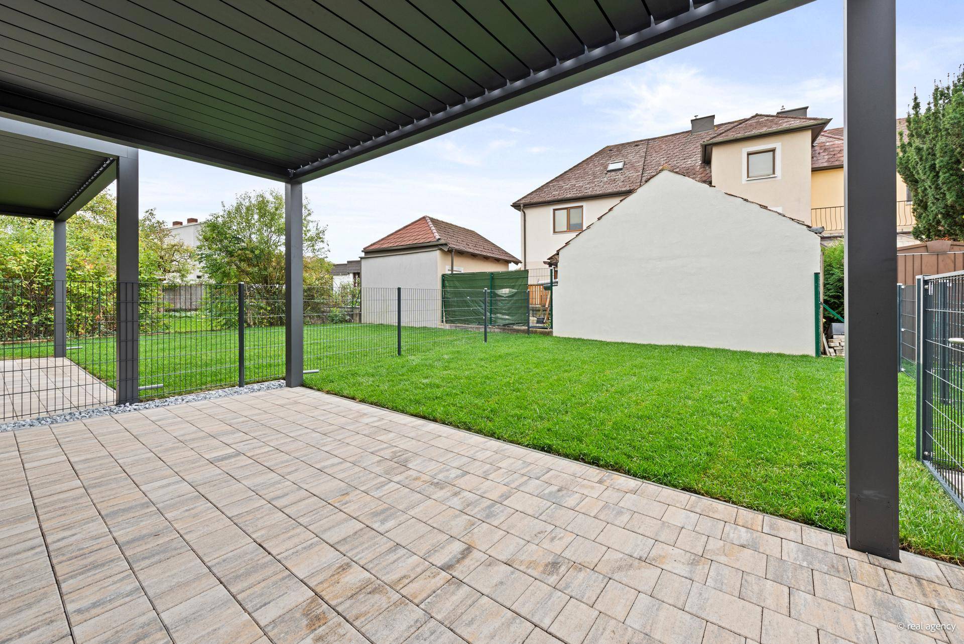 Geräumige, überdachte Terrasse mit Blick auf den eigenen Garten und die umliegende Bebauung.