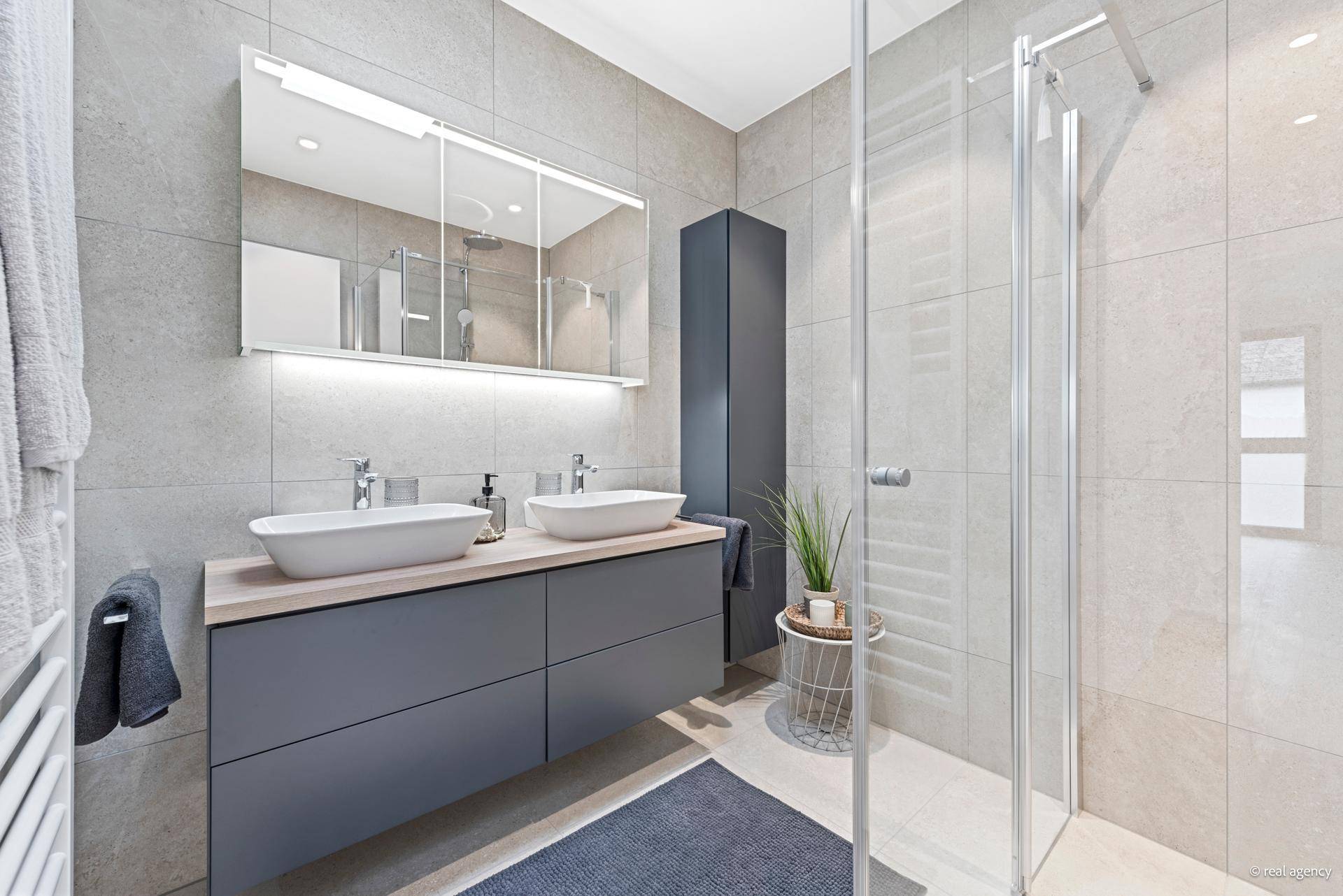 Modernes Badezimmer mit Doppelwaschbecken, großer Dusche und hellen Fliesen.