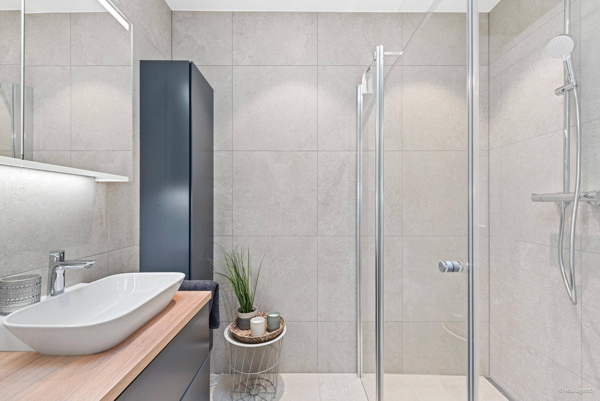Modernes Badezimmer mit Einzelwaschbecken, großer Dusche und eleganten grauen Fliesen.