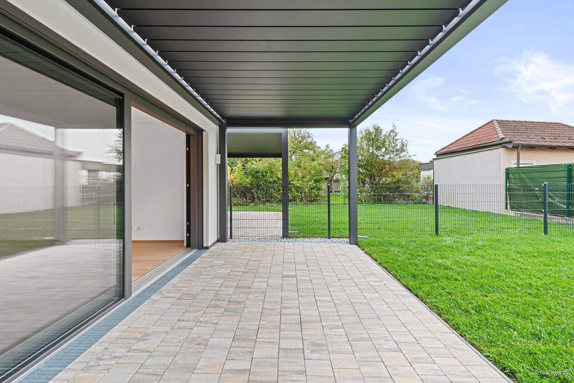 Überdachte Terrasse mit modernen Pflastersteinen und direktem Zugang zum grünen Garten.