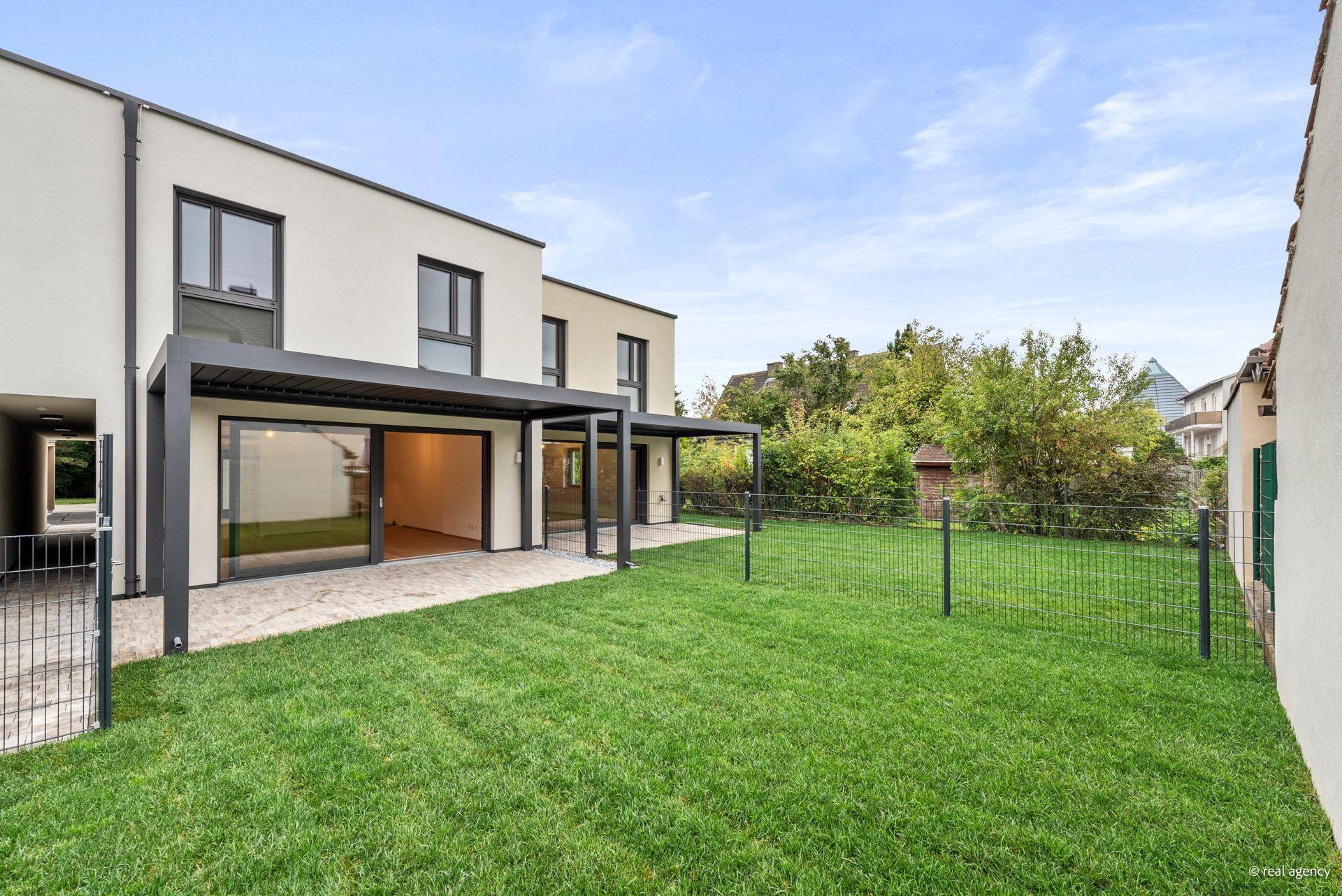 Privater Gartenbereich mit Rasenfläche und überdachter Terrasse, umgeben von grüner Natur.