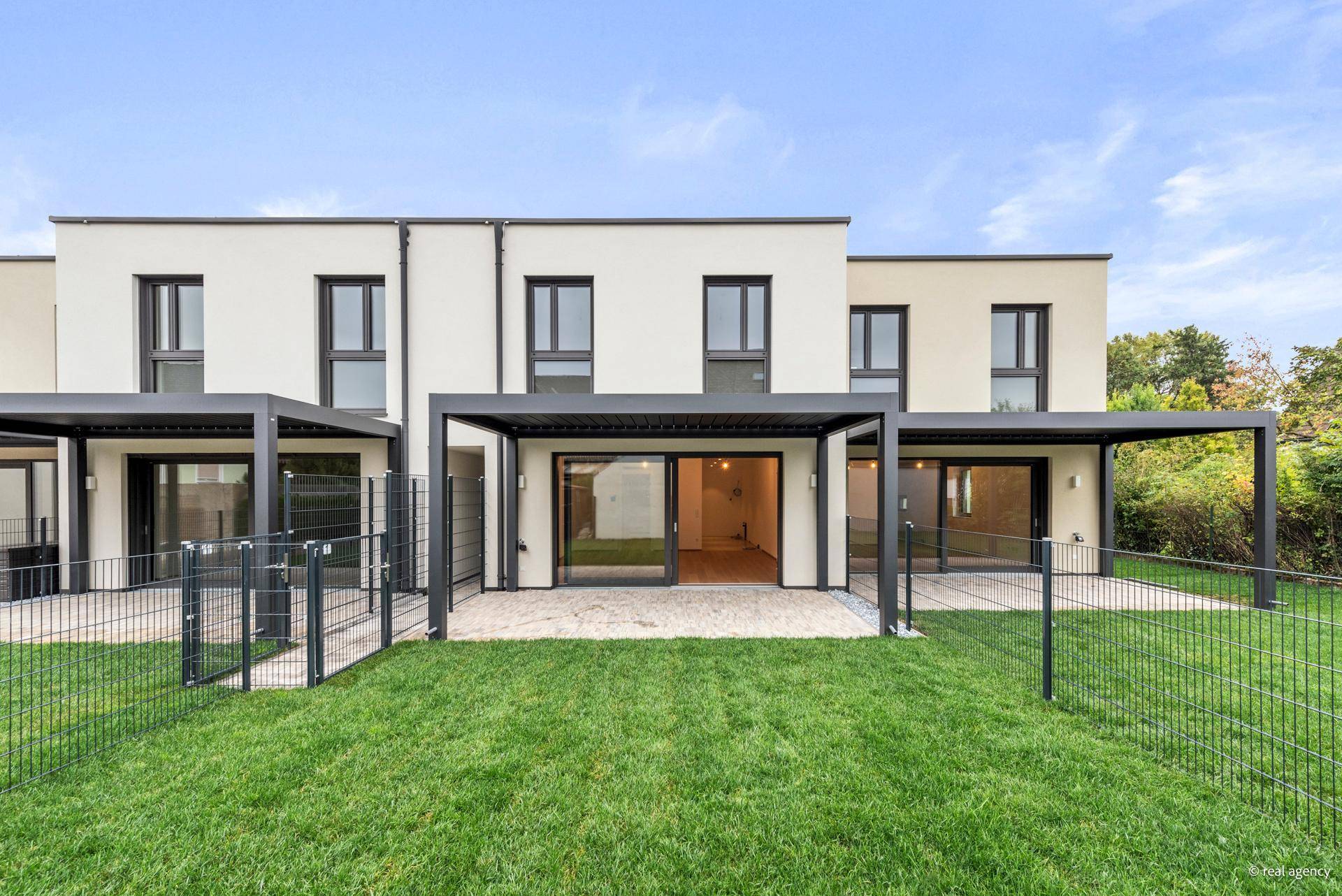 Rückseite der Reihenhäuser mit privaten Gärten, Rasenflächen und überdachten Terrassenbereichen.