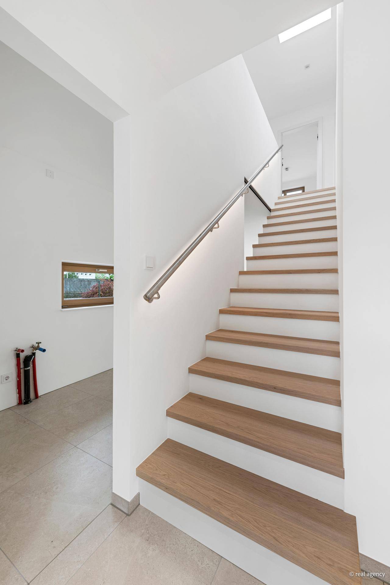 Moderne Holztreppe mit Metallgeländer, die in die oberen Etagen führt, mit viel Tageslicht.