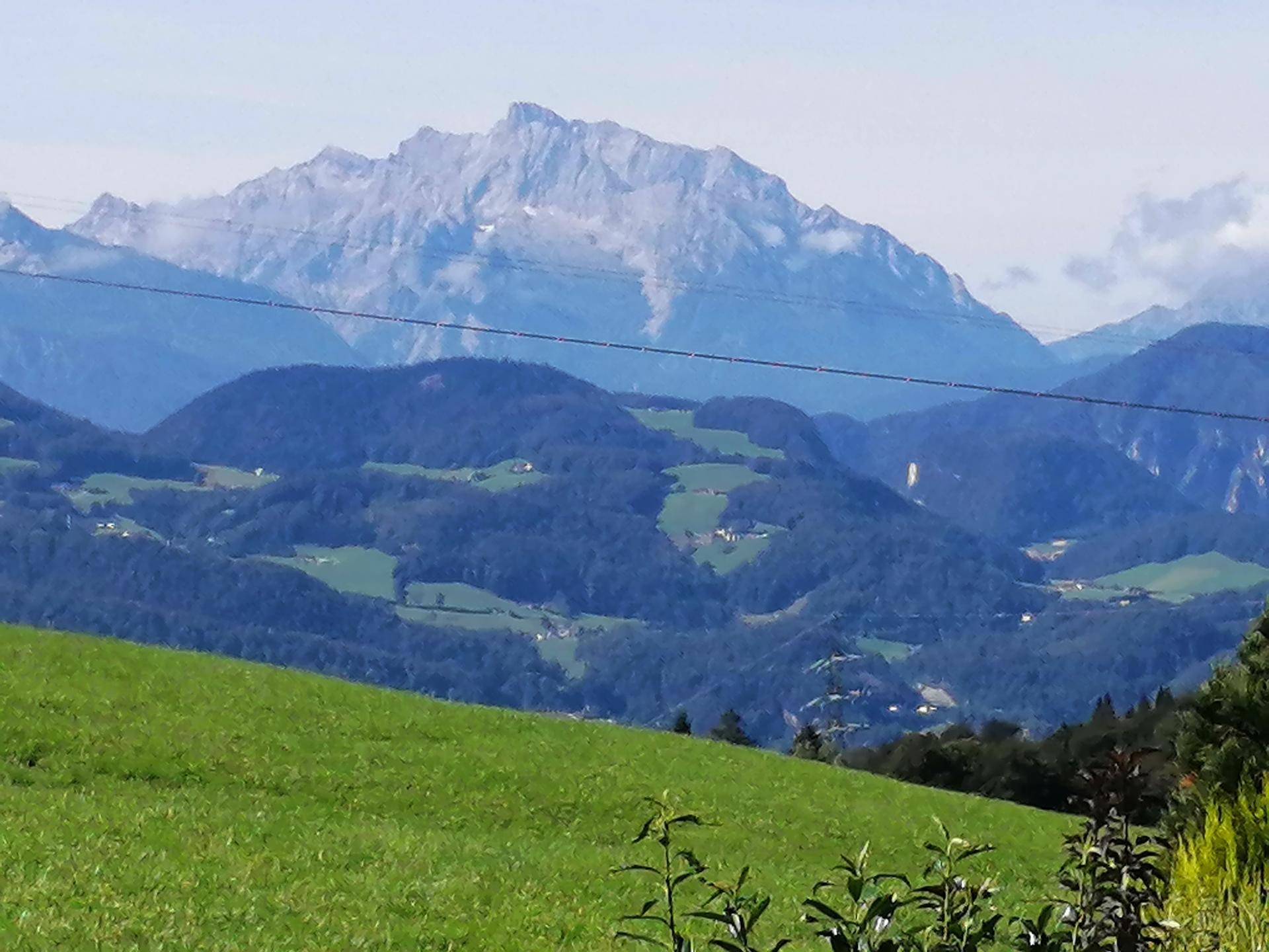 Malerischer Blick auf majestätische Berge und sanfte grüne Hügel unter blauem Himmel.