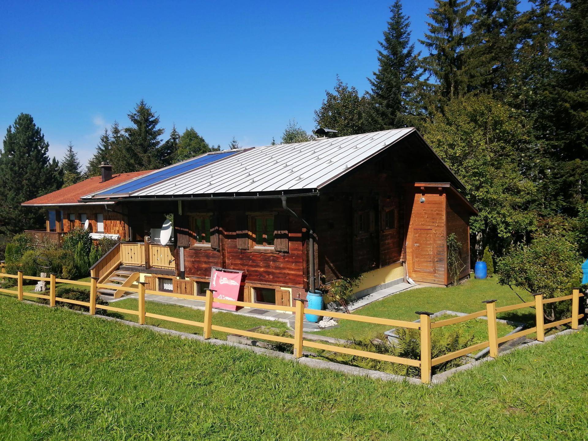 Charmantes Holzhaus im Chalet-Stil mit Solarpaneelen auf dem Dach und umzäuntem Garten.