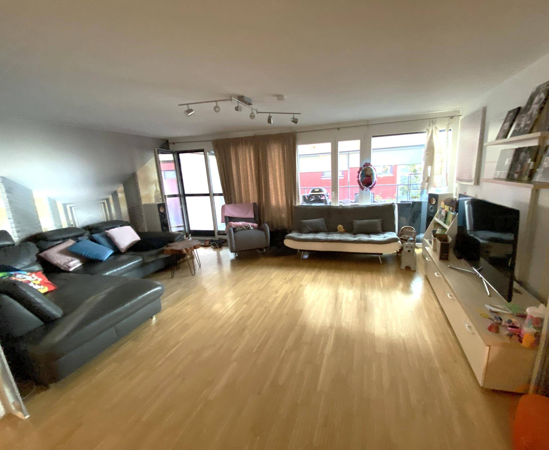 Heller Wohnbereich mit Holzboden, großem Sofa, Medienmöbeln und viel Tageslicht.