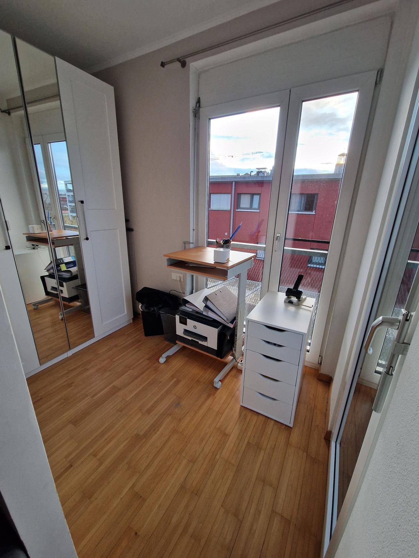 Kleines Arbeitszimmer mit Parkettboden, Spiegelschrank und großen Fenstern.