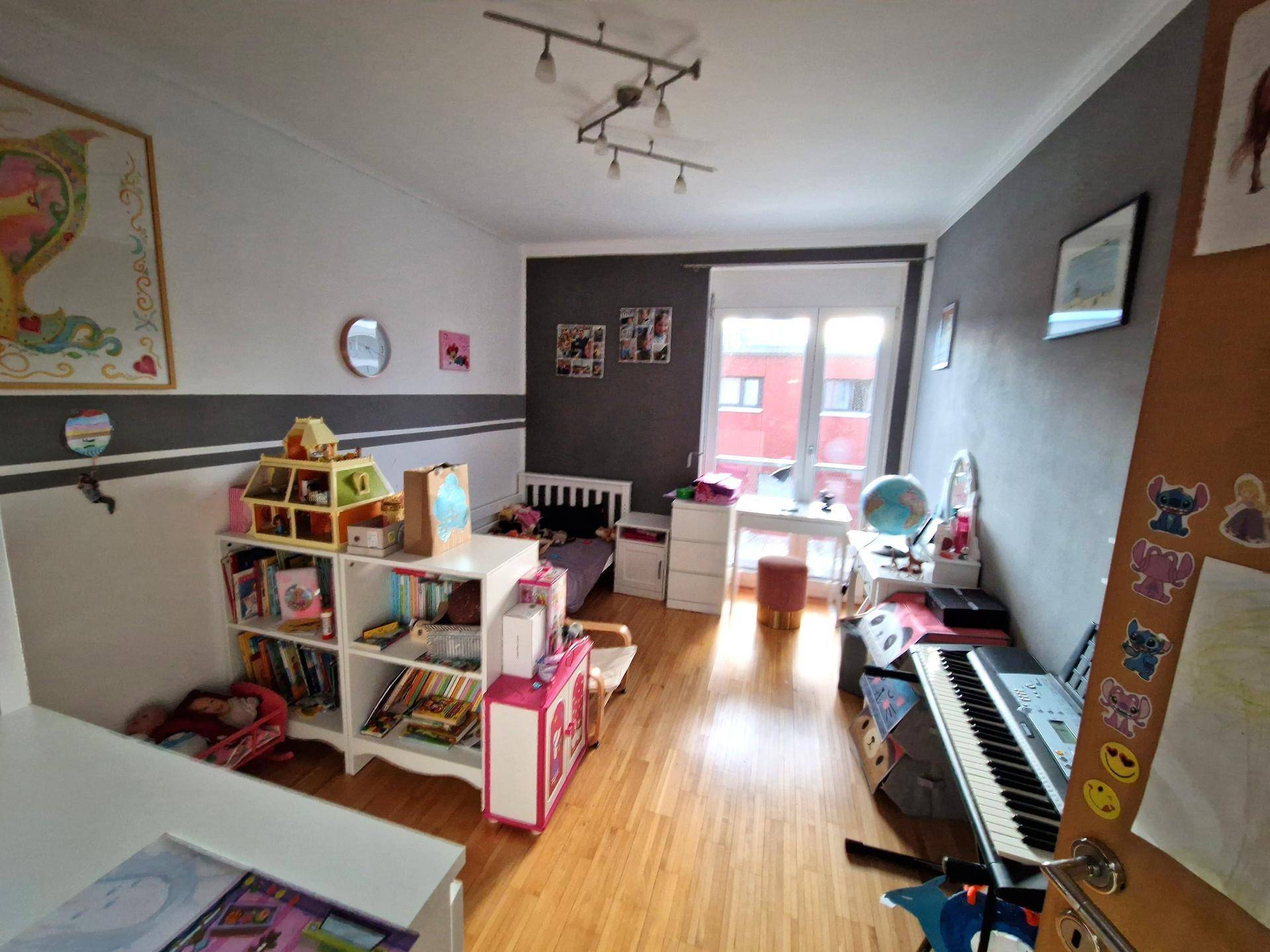 Helles Kinderzimmer mit Parkettboden, Schreibtisch und farbenfroher Dekoration.