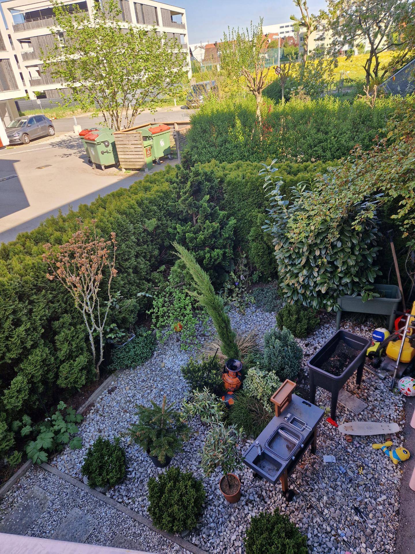 Blick von oben auf den gepflegten Garten mit Kiesflächen, Sträuchern und einem Grillbereich.