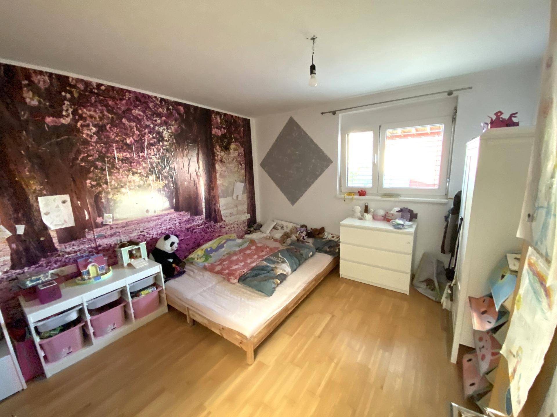 Kinderzimmer mit Holzboden, farbenfroher Wandgestaltung und einem Fenster für natürliches Licht.