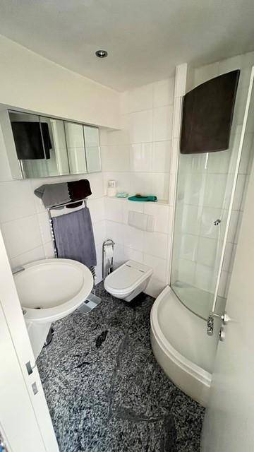 Modernes Badezimmer mit Dusche, WC und Waschbecken, ausgestattet mit dunklem Granitboden und weißen Fliesen.