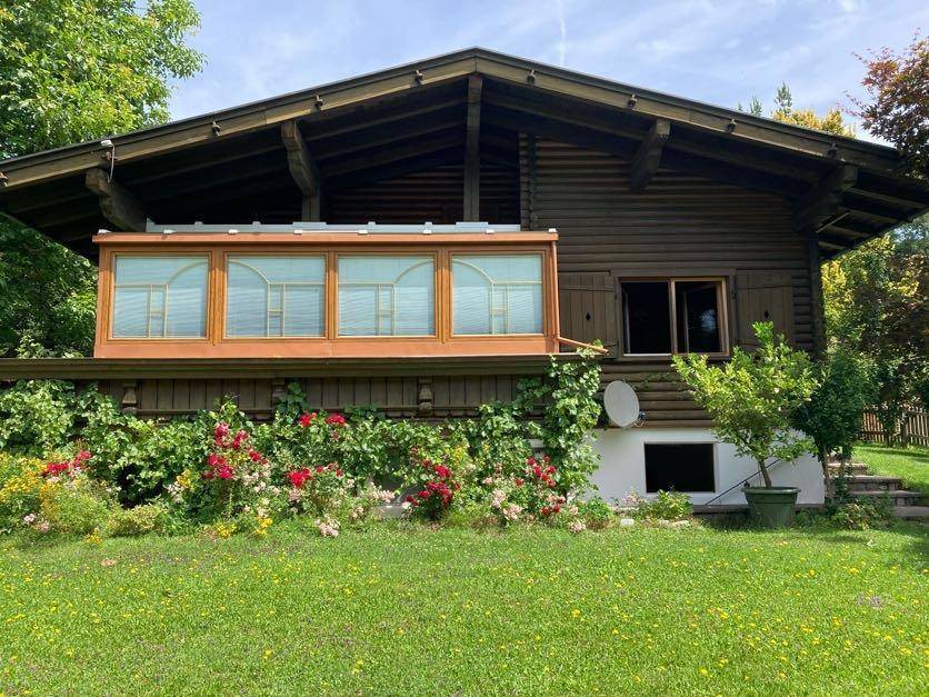 Rustikales Holzhaus mit breiter Fensterfront und blühenden Sträuchern im Vorgarten.