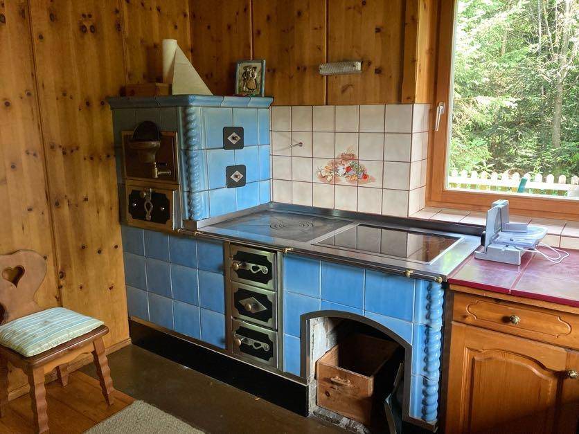 Rustikale Küche mit blauem Kachelofen als Kochstelle und Holzvertäfelung an den Wänden.