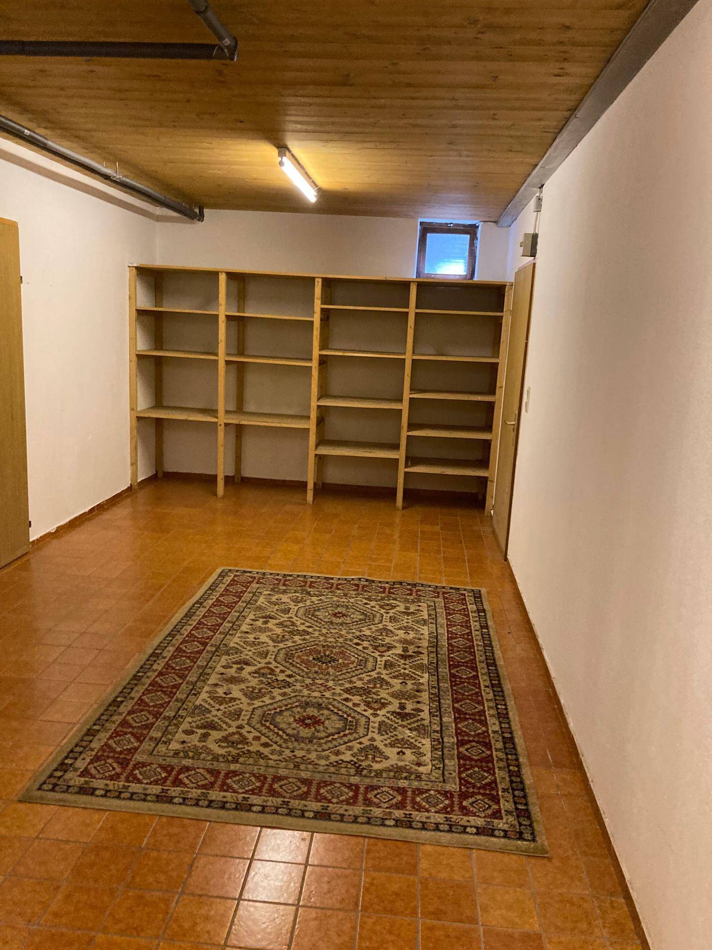 Geräumiger Abstellraum mit Holzregalen, Teppich und kleinem Fenster für Tageslicht.