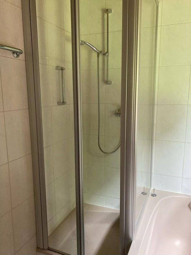 Duschbereich mit Glasabtrennung und weiß gefliesten Wänden im Badezimmer.