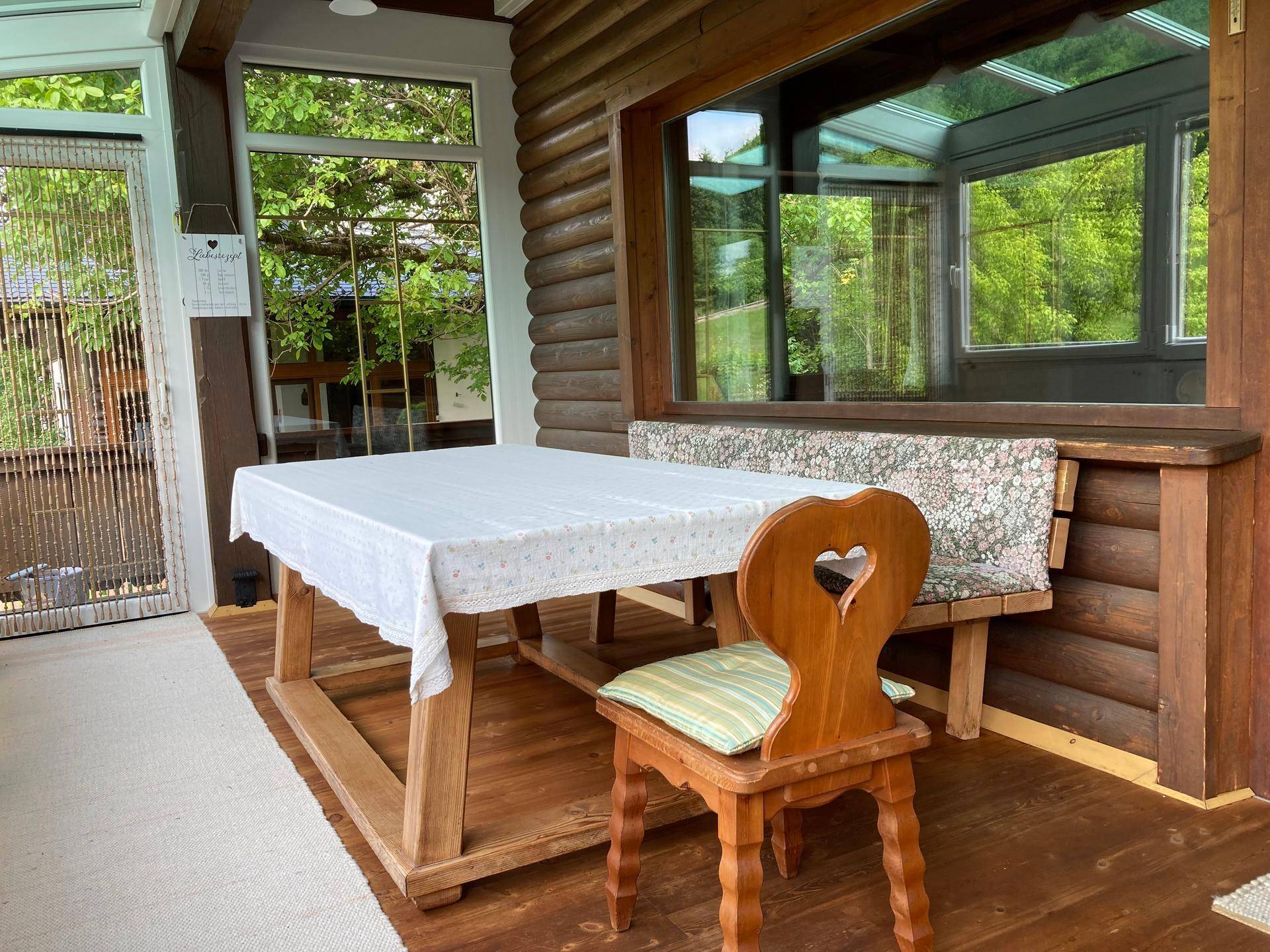 Gemütlicher Wintergarten mit Holztisch, Bank und weitem Blick auf die Natur.