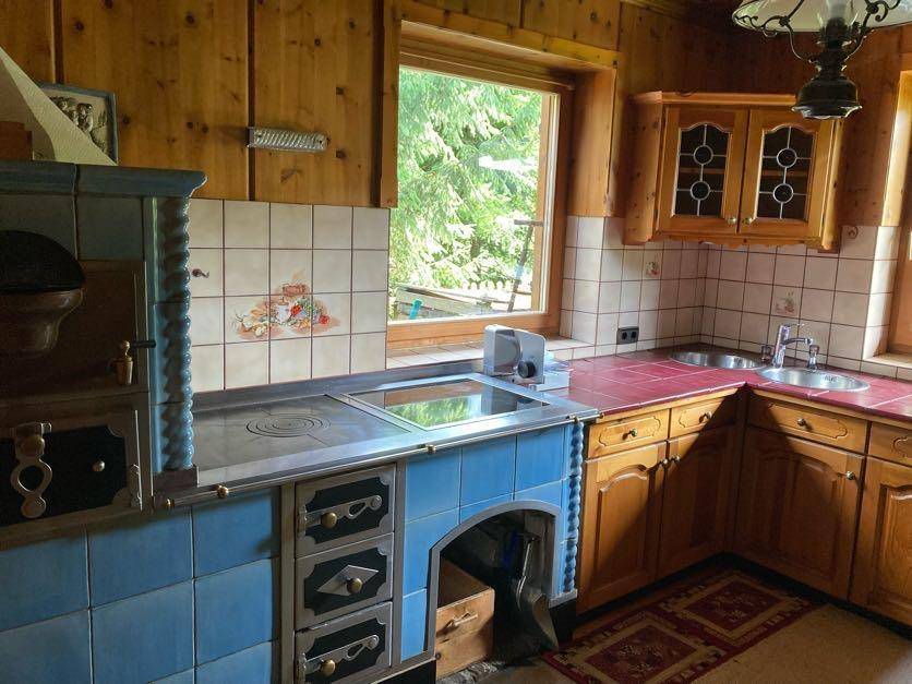 Traditionelle Küche mit Holzvertäfelung, blauem Kachelofen und rustikalen Schränken.