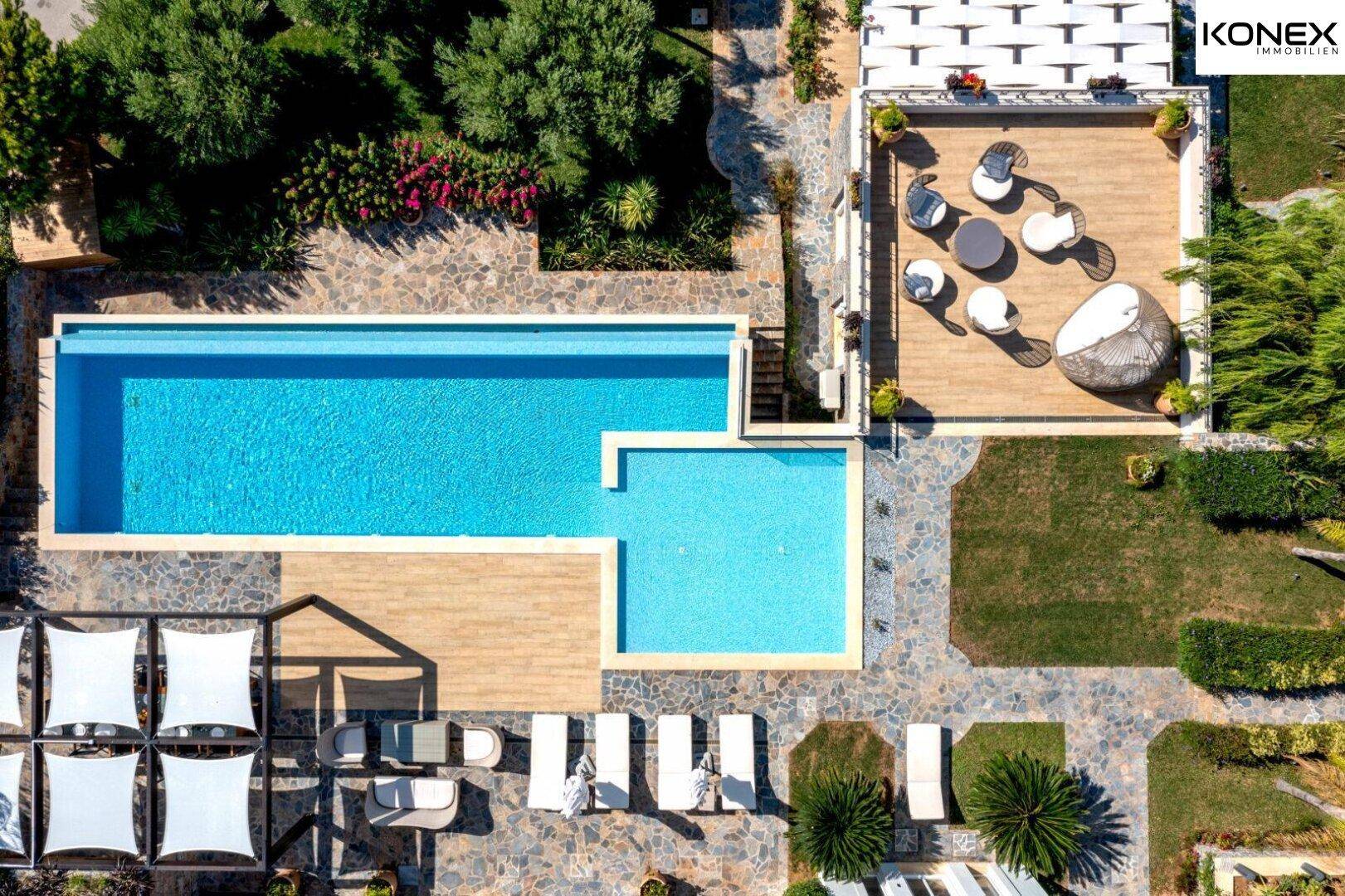 Detailansicht des weitläufigen Poolbereichs mit Holzdeck, Liegestühlen und schattenspendenden Segeln.