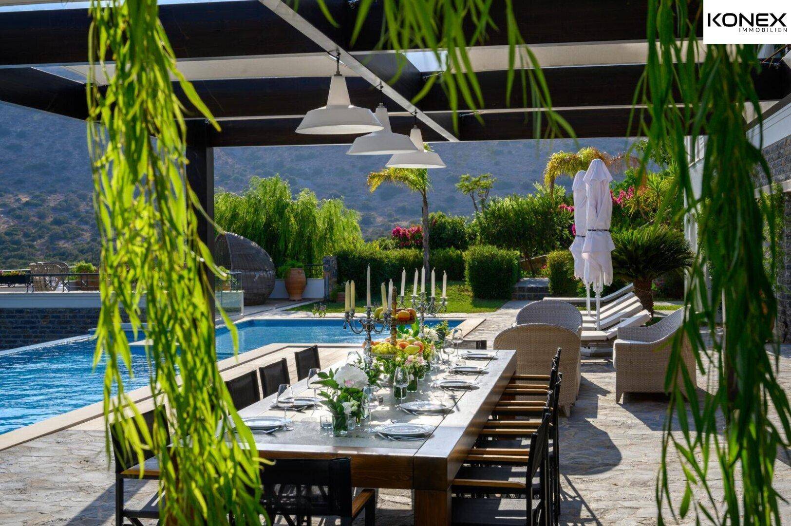 Überdachter Essbereich im Freien mit großem Tisch, Kronleuchtern und Blick auf den Pool.