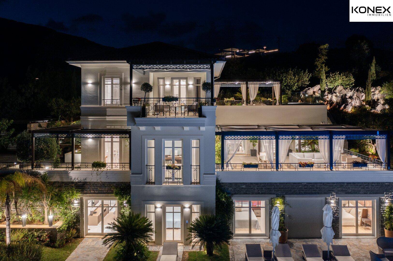Beleuchtete Fassade der Villa bei Nacht mit mehreren Balkonen und Terrassen.