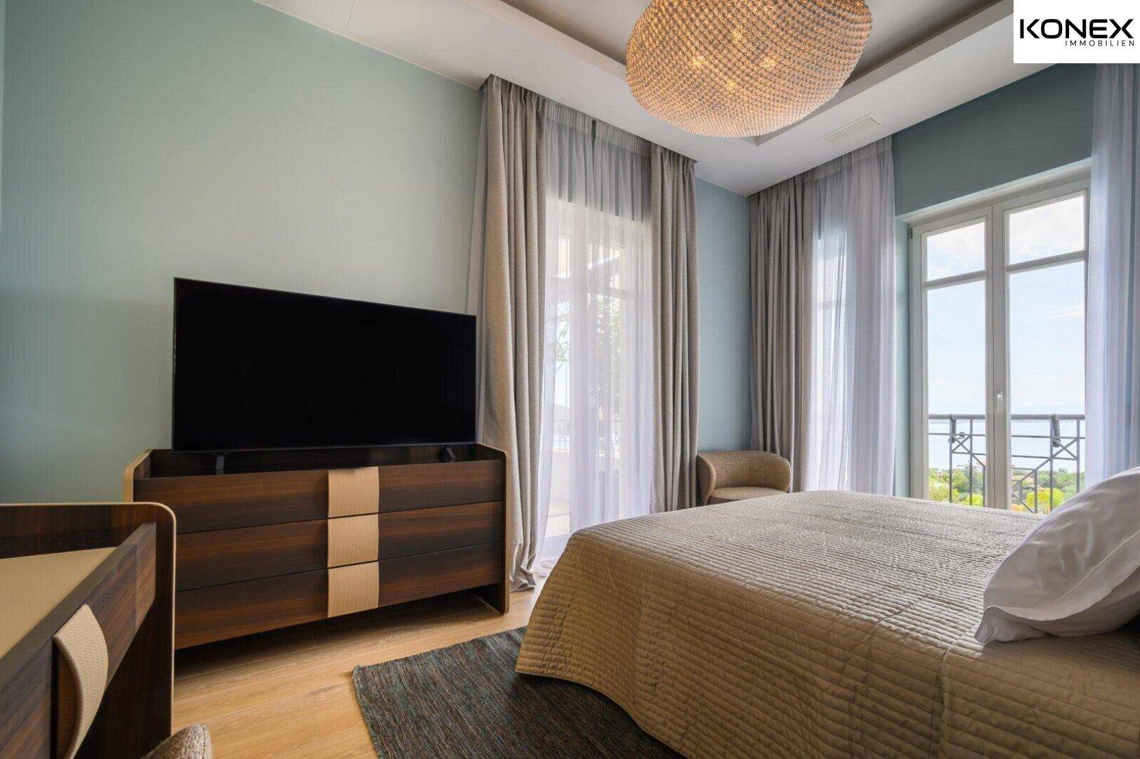 Helles Schlafzimmer mit Holzboden, großem Fernseher und Blick auf die Umgebung.