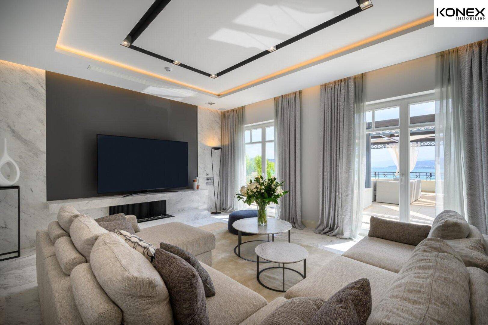 Heller Wohnbereich mit großem Sofa, Fernseher und direktem Zugang zu einer Terrasse mit Meerblick.