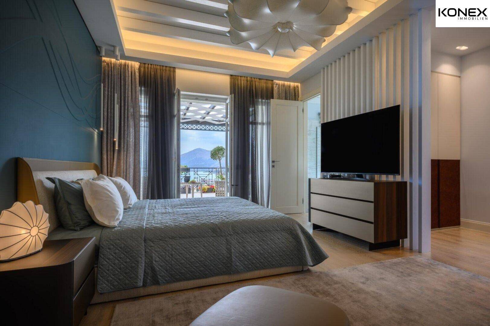 Modernes Schlafzimmer mit Holzboden, großem Bett und Zugang zu einem Balkon mit Meerblick.