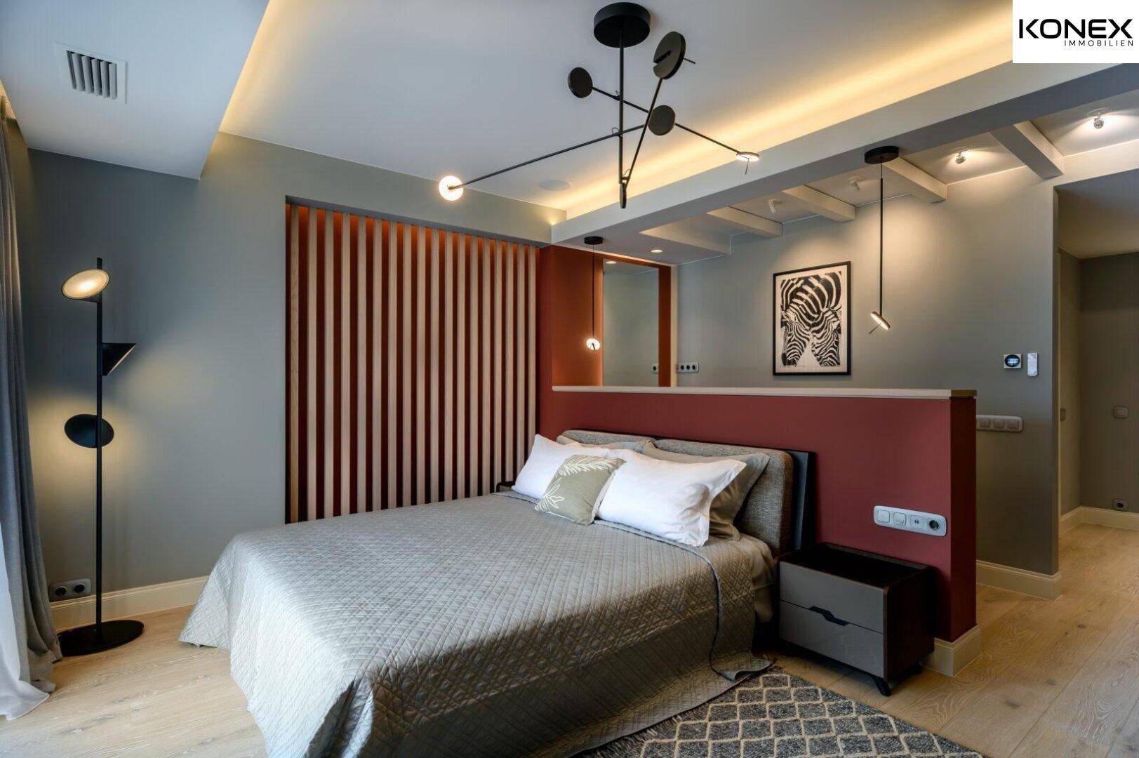 Elegantes Schlafzimmer mit Holzboden, roter Akzentwand und stilvoller Beleuchtung.