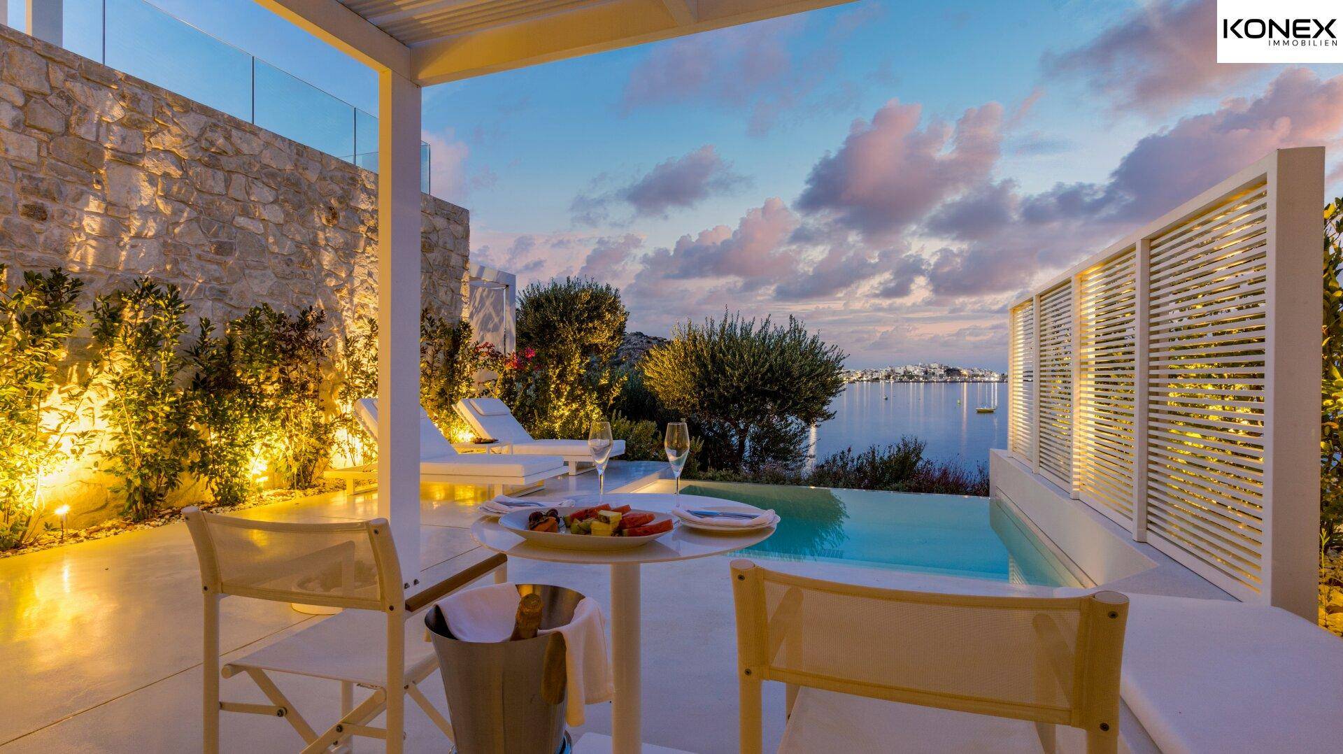 Gemütlicher Essbereich im Freien neben einem privaten Pool mit Meerblick bei Sonnenuntergang.