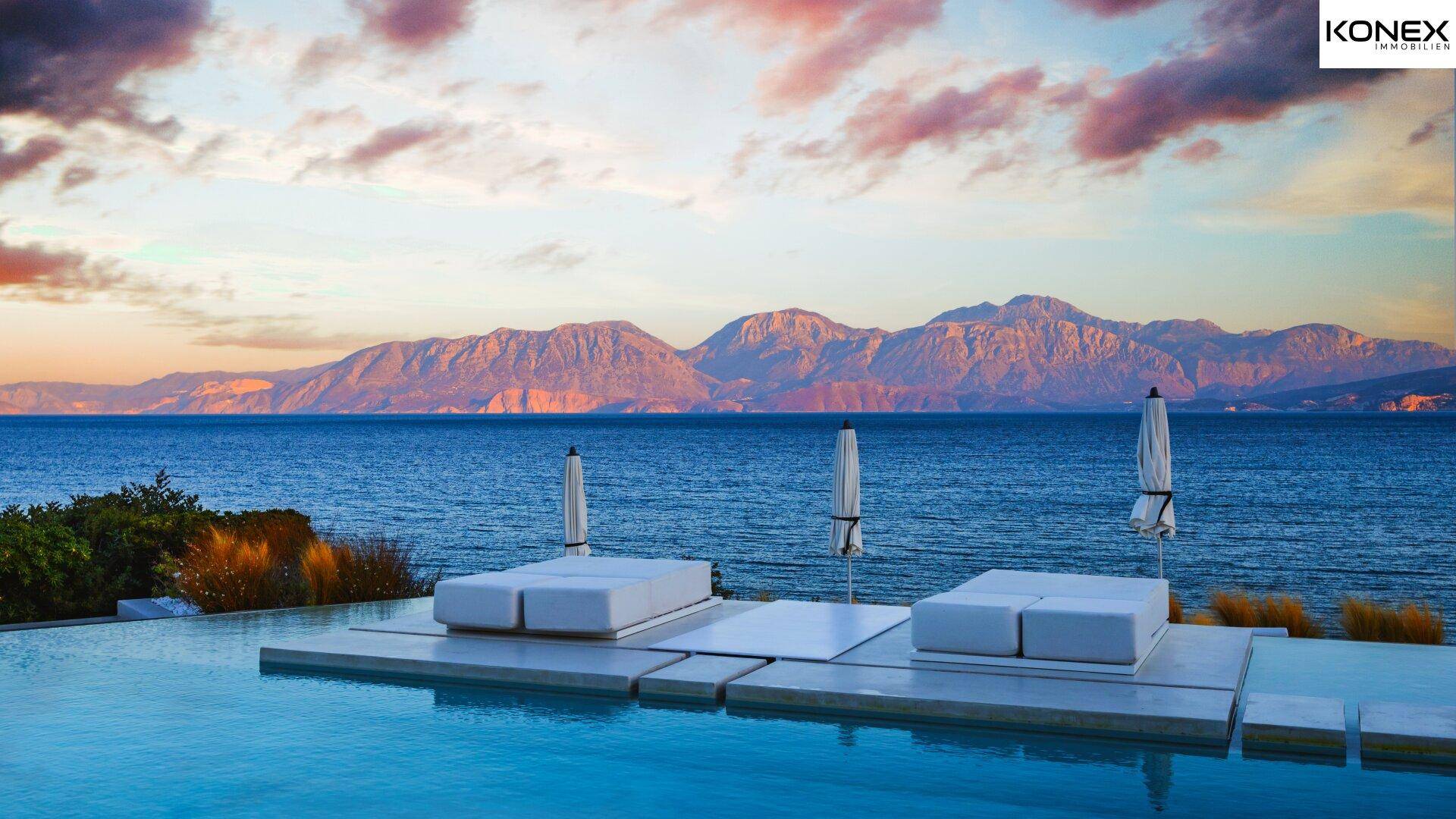Infinity-Poolbereich mit luxuriösen Liegen und atemberaubendem Blick auf das Meer und die Berge bei Sonnenuntergang.