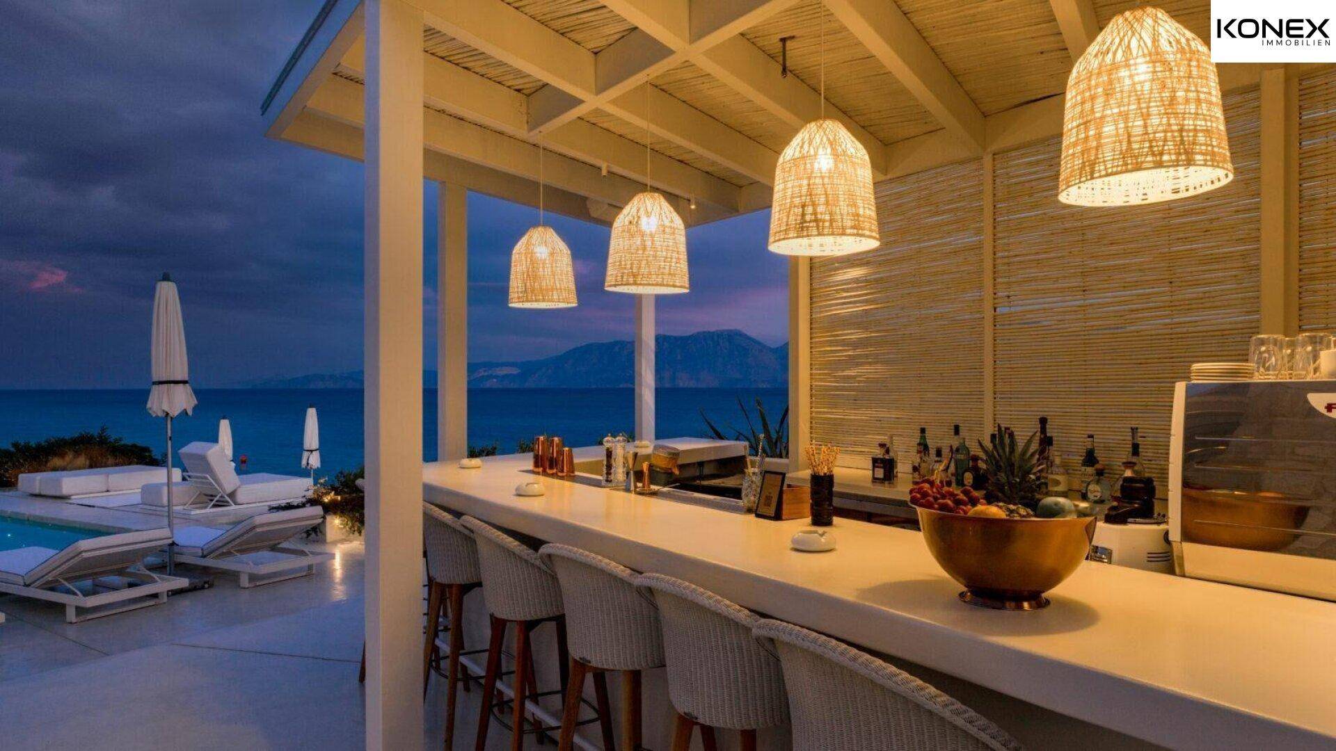 Elegante Bar mit Rattan-Hockern und Meerblick, perfekt für abendliche Cocktails am Pool.