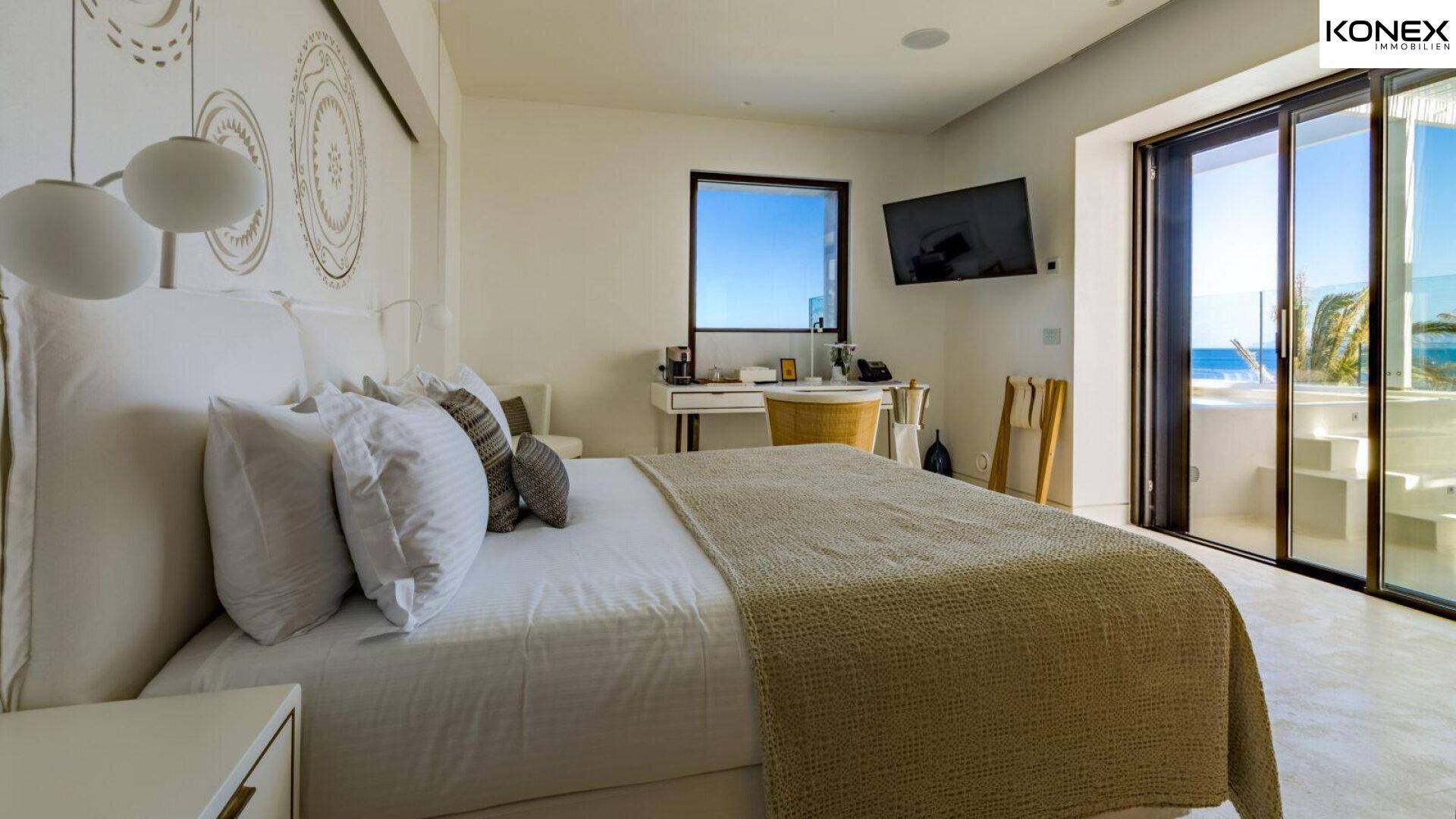 Modernes Schlafzimmer mit großem Bett, Schreibtisch und Fenster mit atemberaubendem Meerblick.