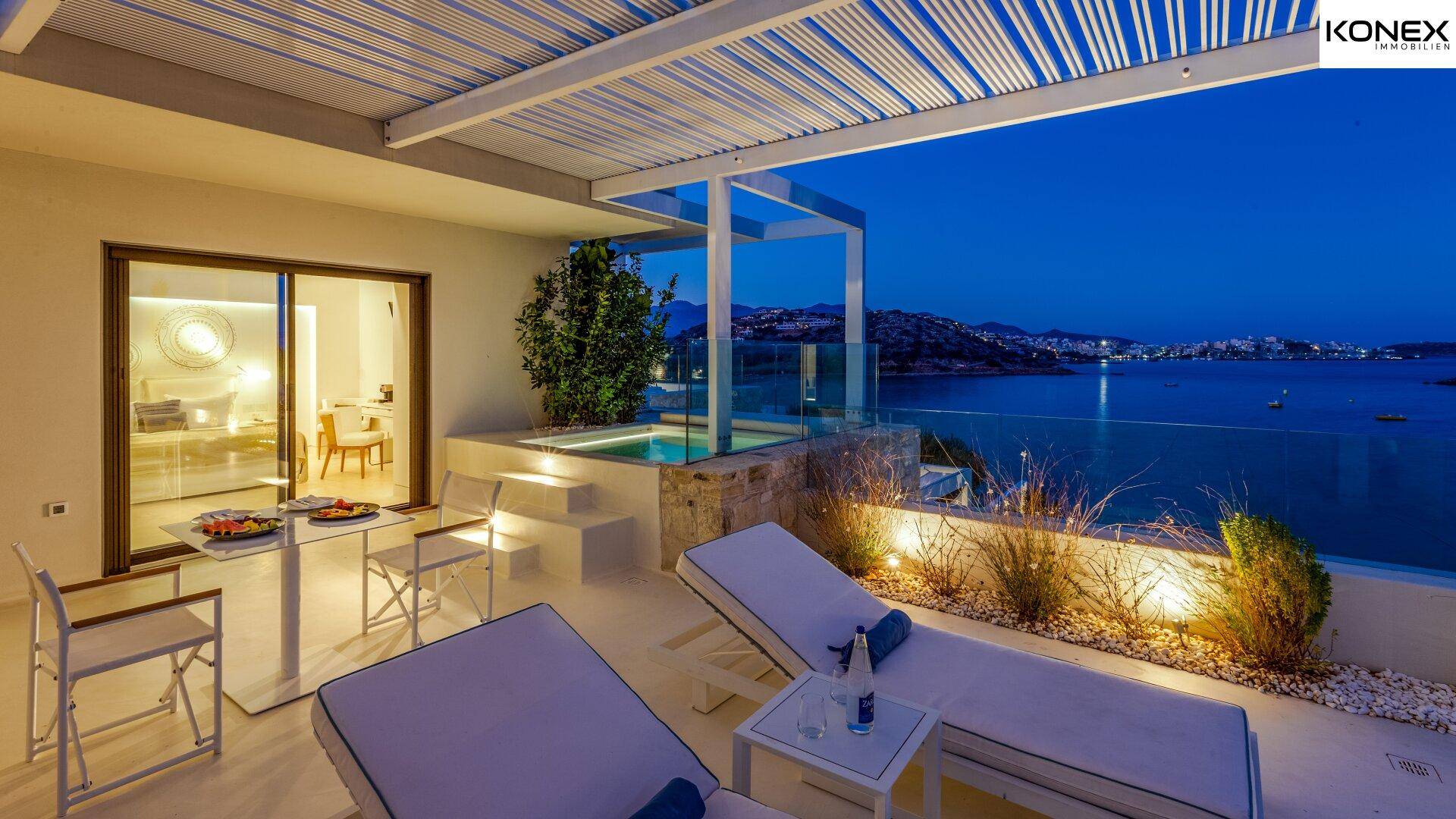 Private Terrasse mit kleinem Pool und Liegen bei Nacht, bietet einen romantischen Meerblick.