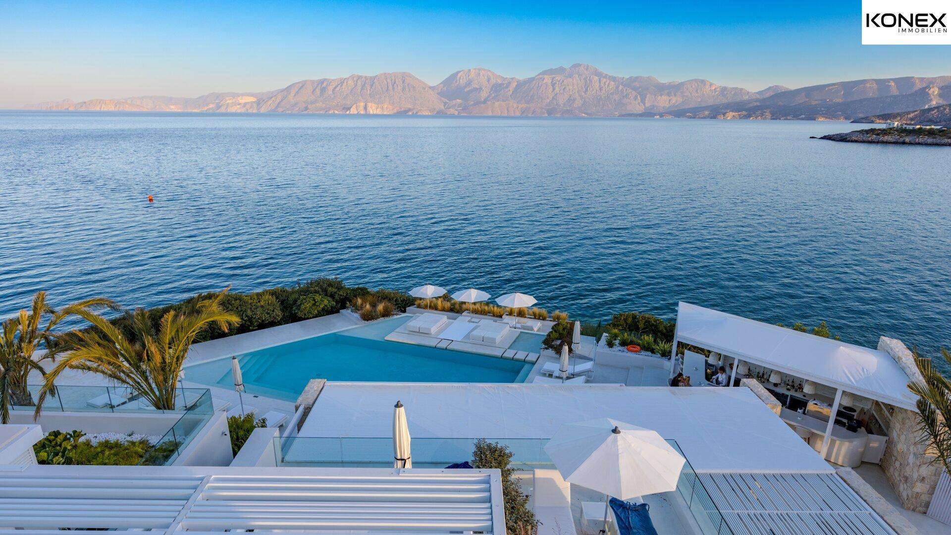 Weitläufiger Poolbereich und moderne Gebäude mit Panoramablick auf das Meer und die Berge.