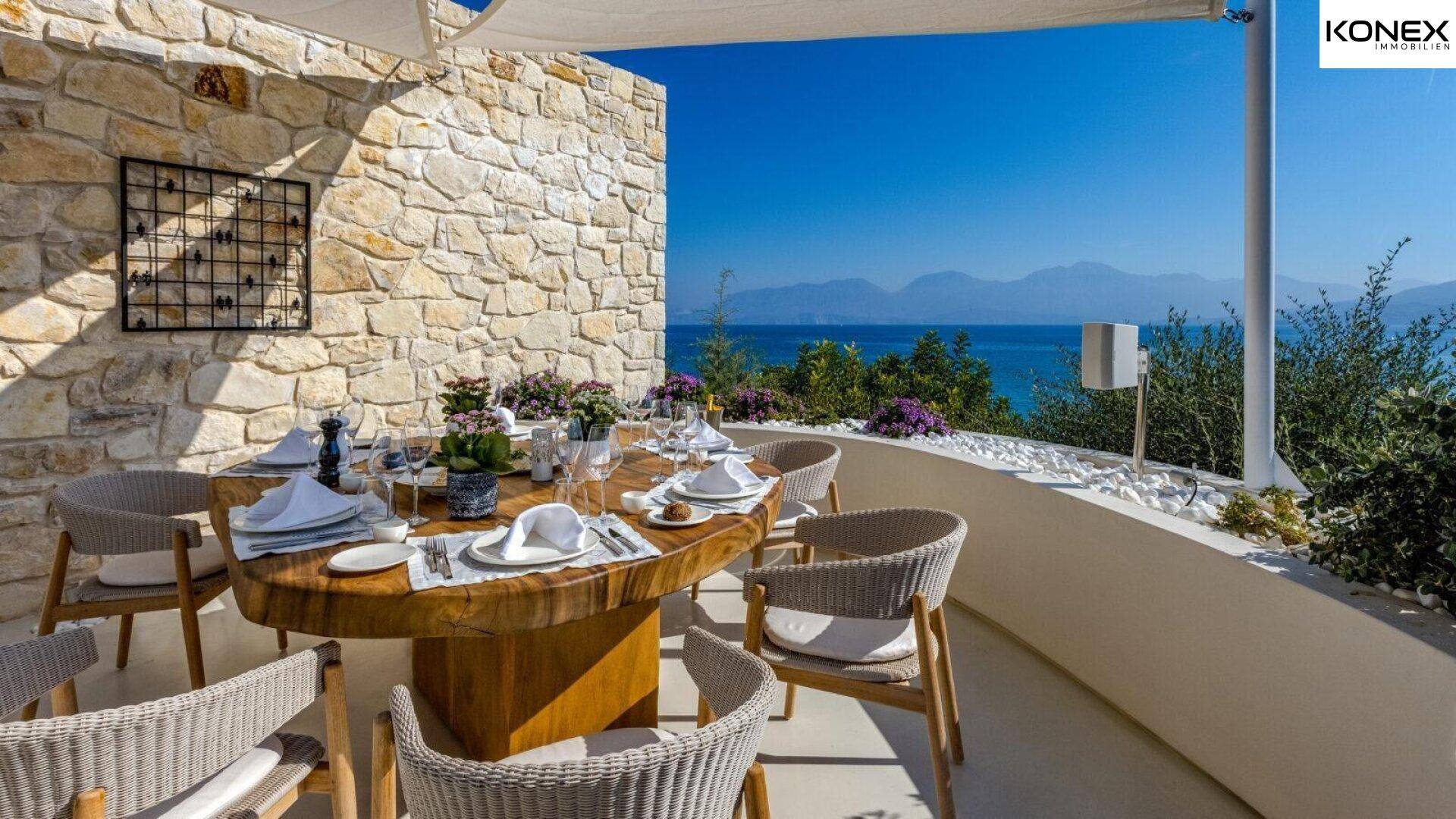 Einladender Essbereich im Freien auf einer Terrasse mit Steinwand und weitem Meerblick.