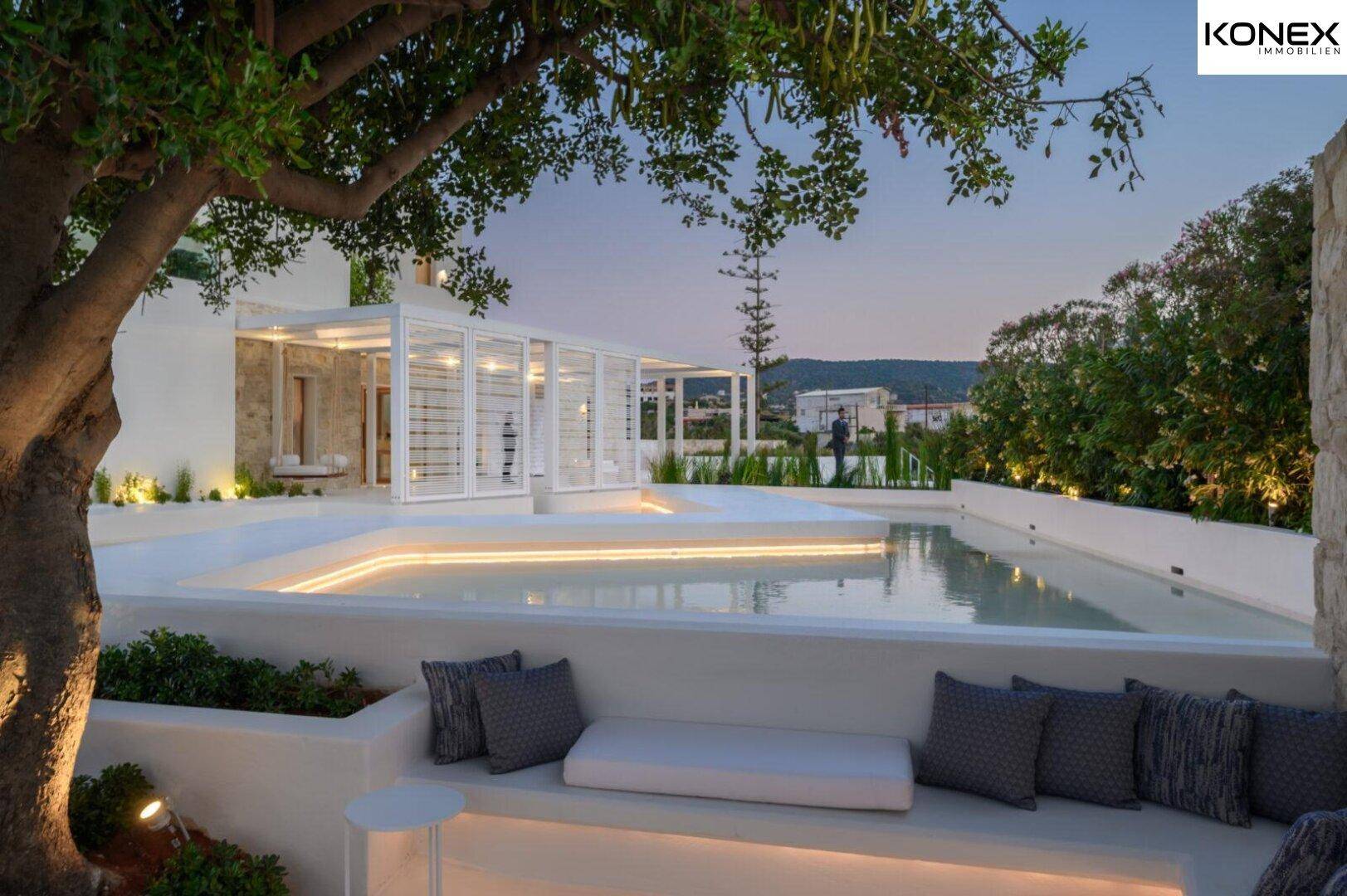 Entspannender Lounge-Bereich im Freien mit flachem Pool und üppiger Bepflanzung bei Dämmerung.