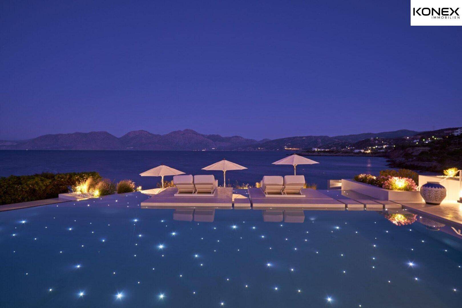 Beleuchteter Infinity-Pool mit Sternenlichtern und weitem Meerblick in der Nacht.
