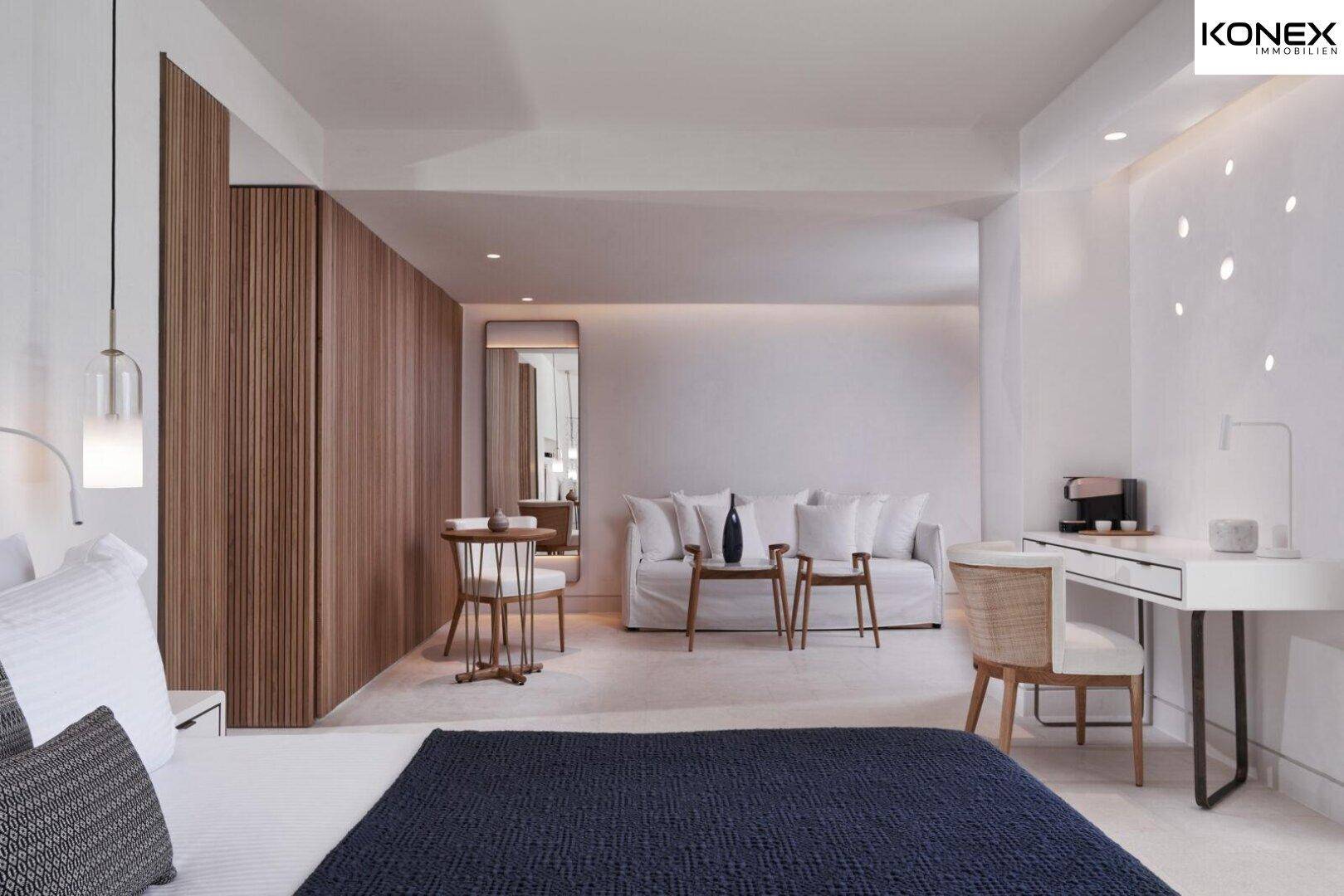 Geräumiges, modernes Schlafzimmer mit großem Bett, Sofa und Arbeitsbereich in hellen Farben.